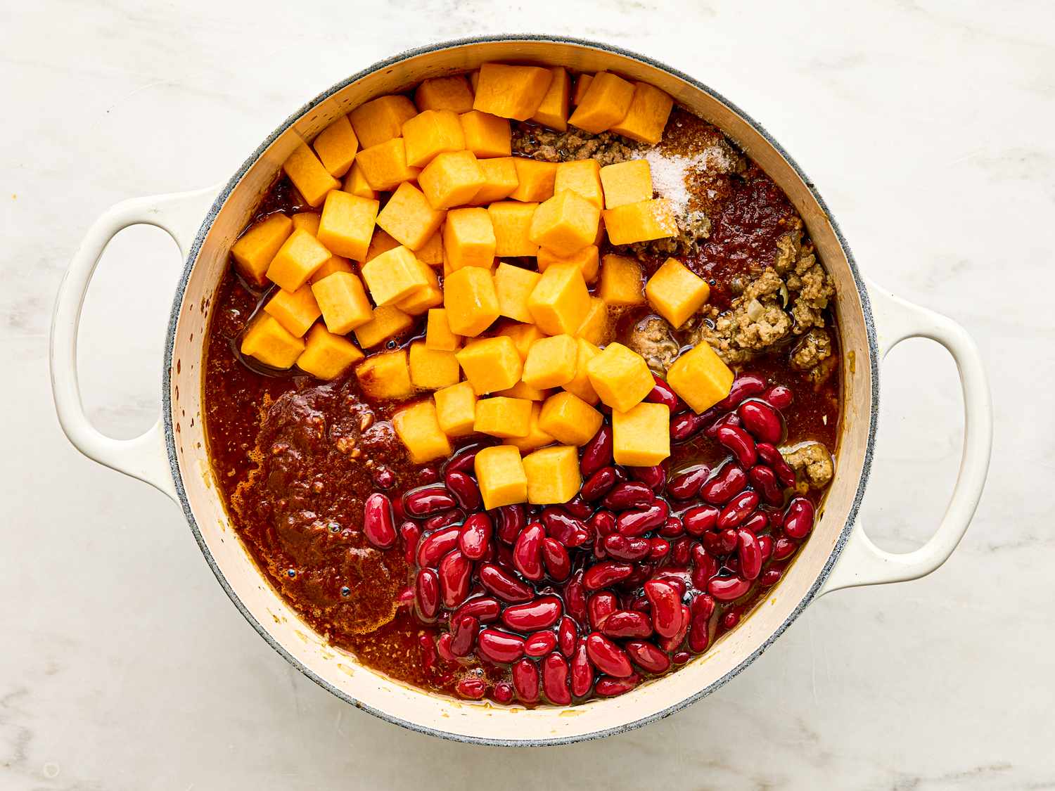 A pot containing turkey chili ingredients such as ground meat diced squash kidney beans and tomato base