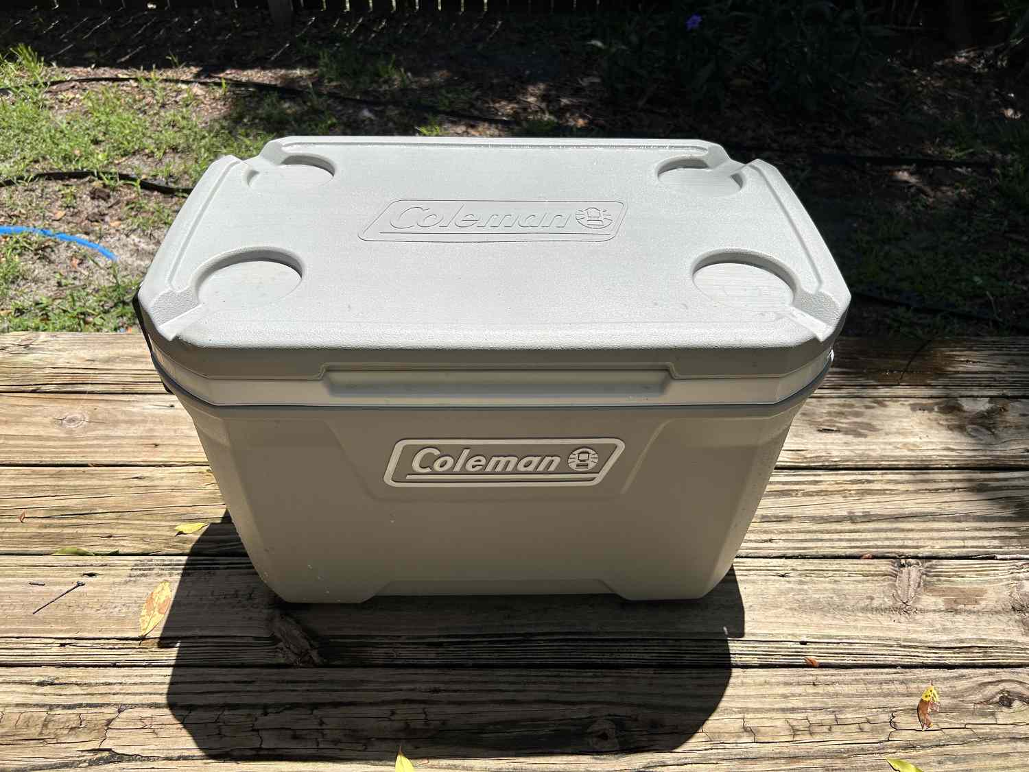 A grey Coleman cooler with its lid closed sitting on a deck.