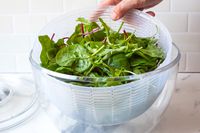 placing a bowl of greens in the plastic oxo spinner