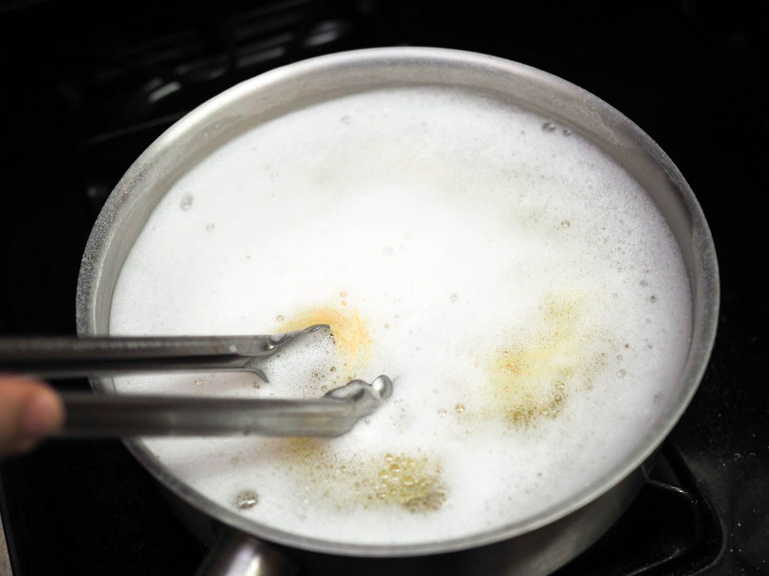 Stirring a pot of angel hair pasta in seasoned water with a pair of tongs. 