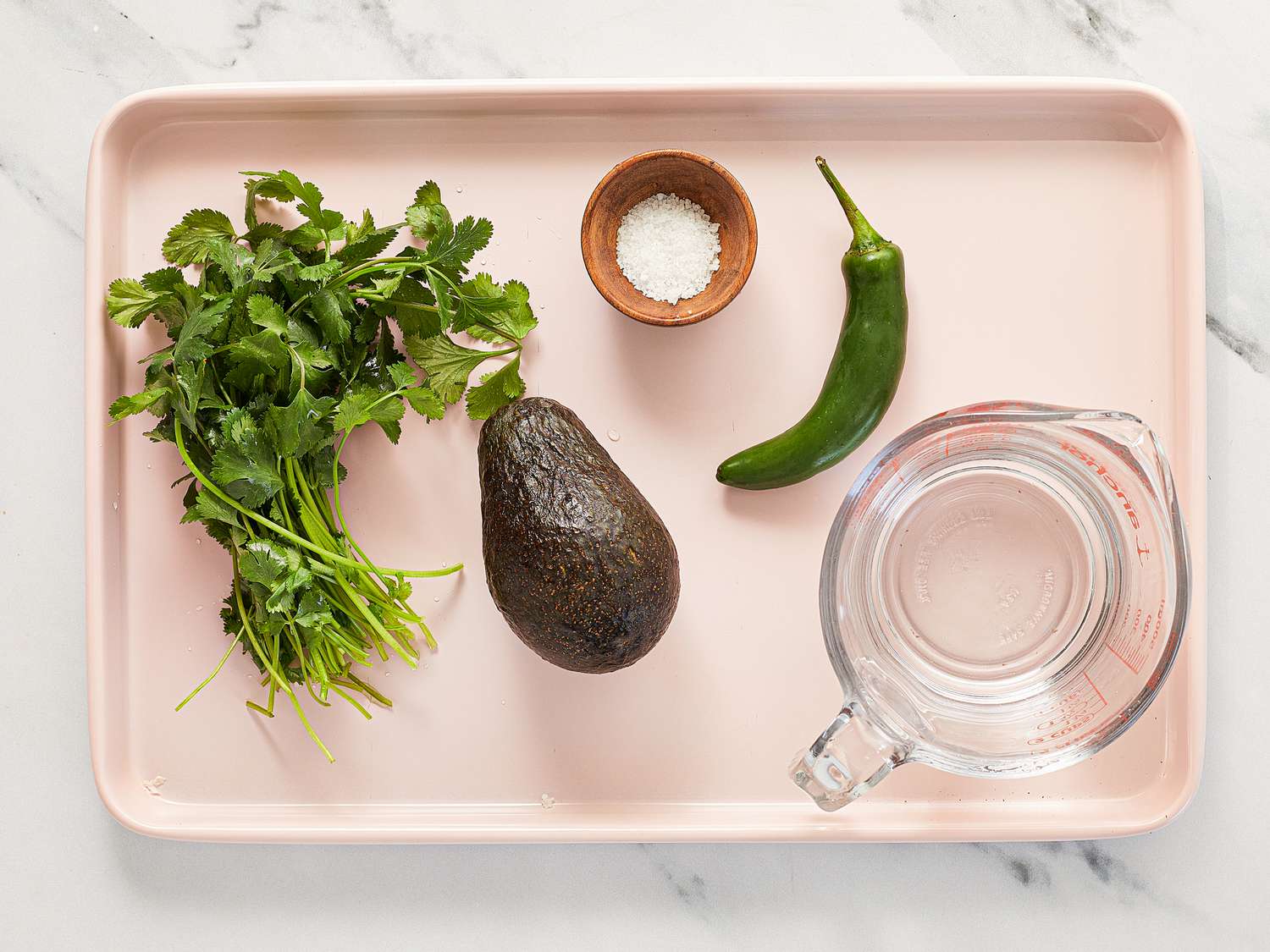 mise en place of measuring cup, cilantro, avocado, pepper and salt on a tray