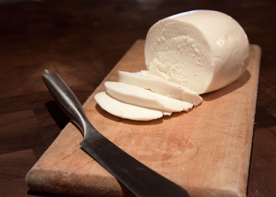 A ball of fresh mozzarella, partially sliced on a wooden board with a knife.