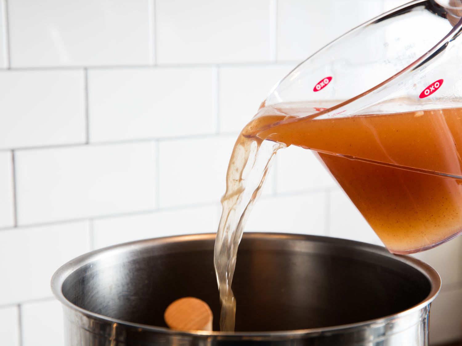 Meat broth being pouring into a stock pot.
