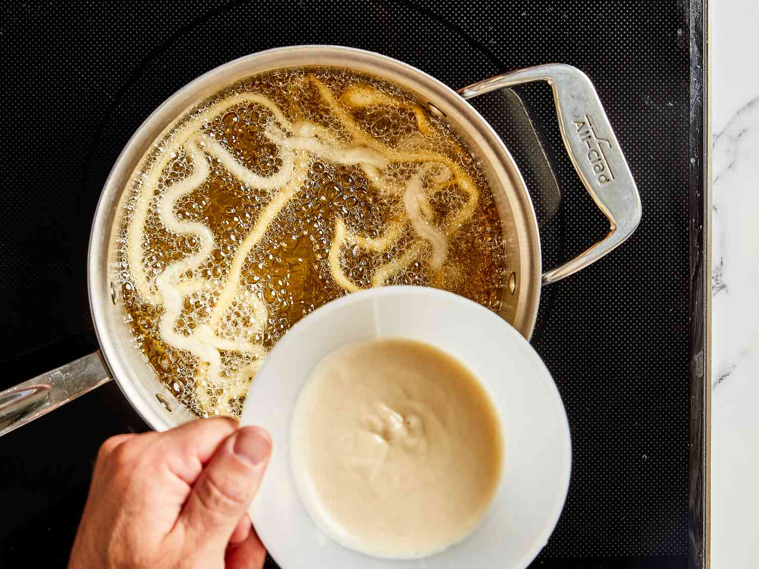 Overhead view of using funnel to pour batter directly into oil