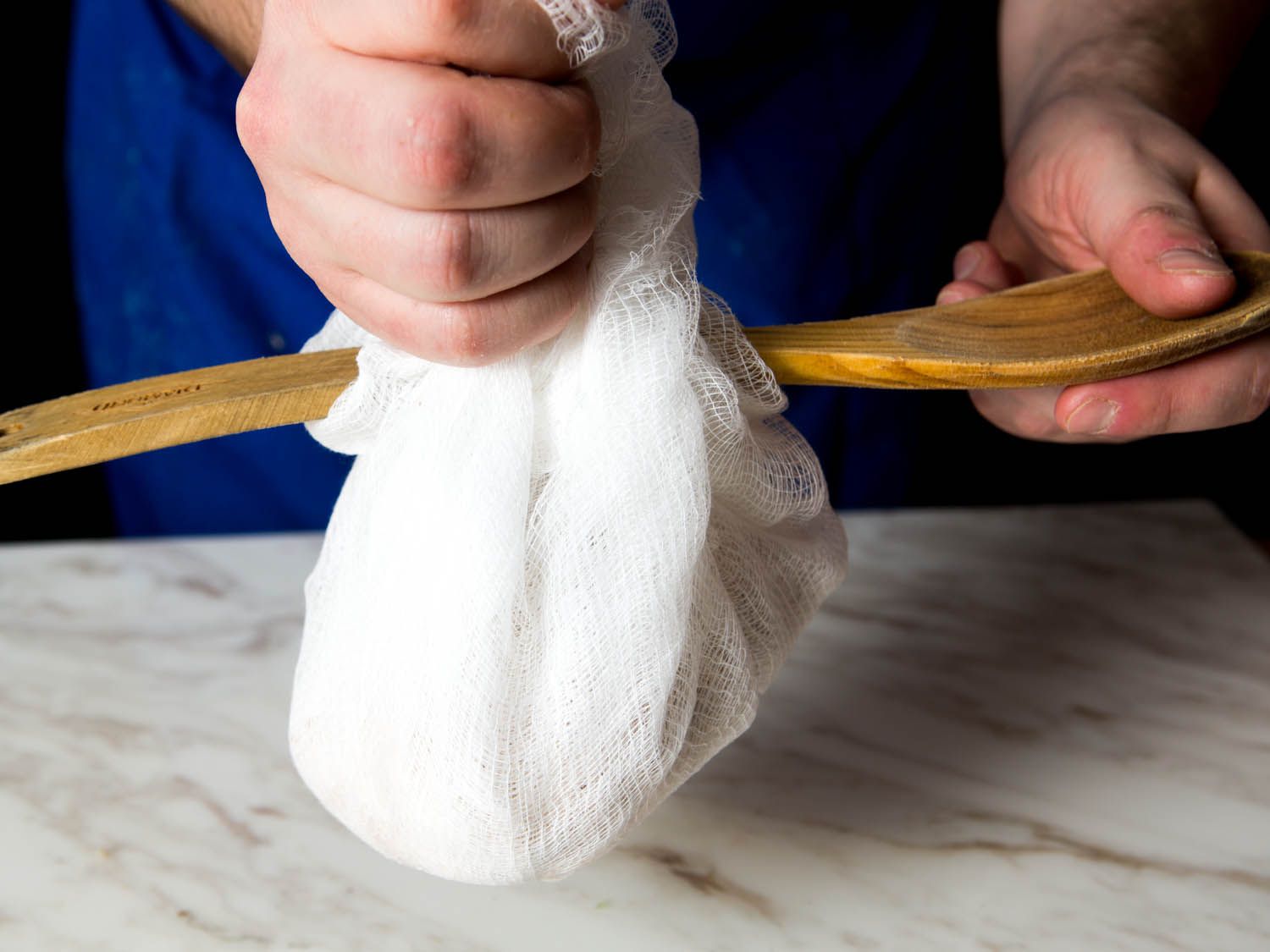 Holding the ends of a bundle of cheesecloth, wrapped around the handle of a wooden spoon.