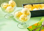 Scoops of mango ice cream in glass bowls with an ice cream tub in the background