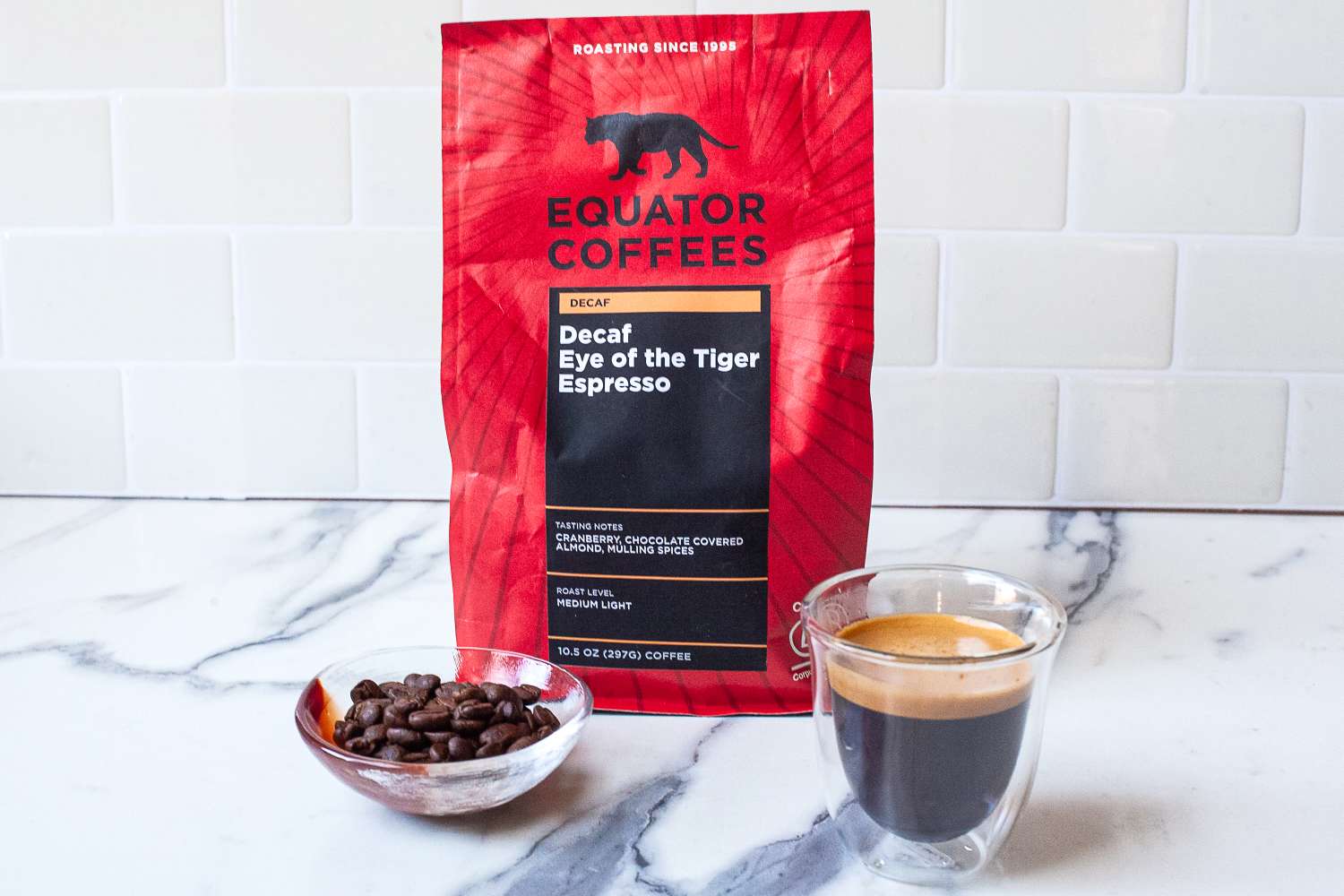 A coffee bag labeled Equator Coffees, a bowl of coffee beans, and an espresso shot in a glass cup