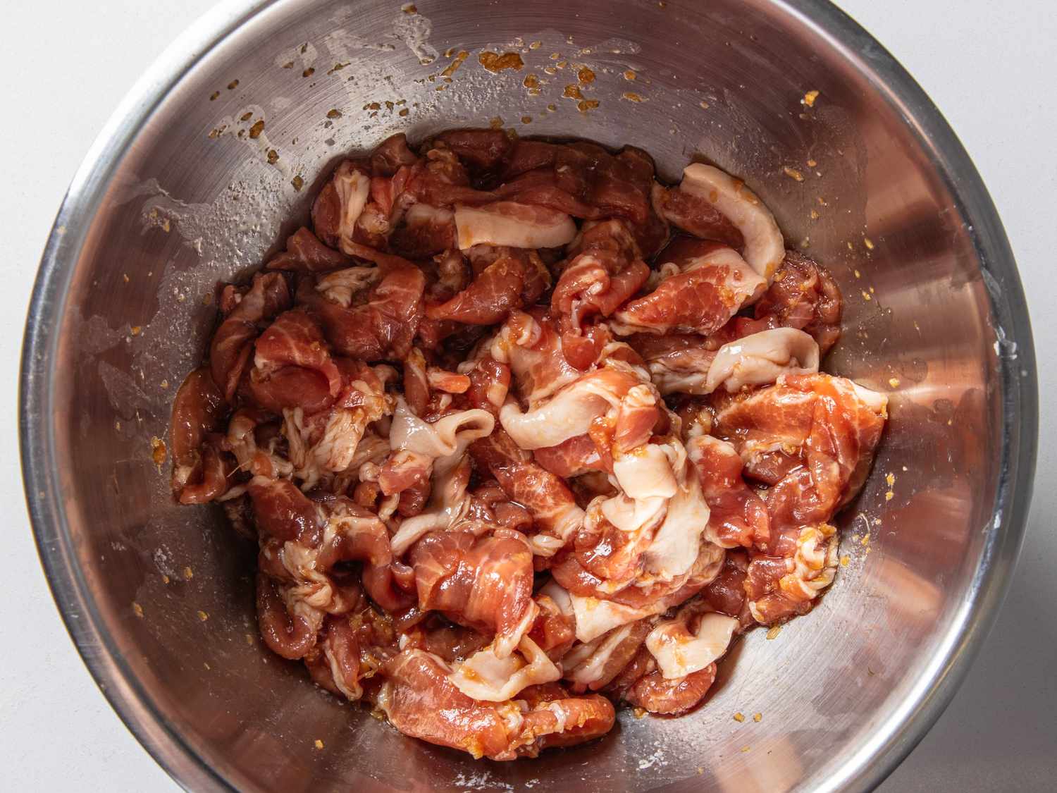 Thinly sliced pork marinating in a bowl with soy sauce, mirin, sake, and grated garlic