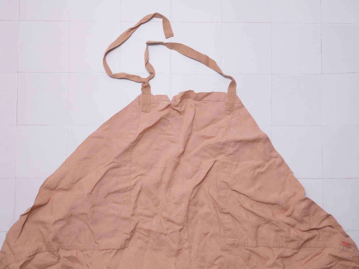 a closeup of a pink linen apron on a white tile surface