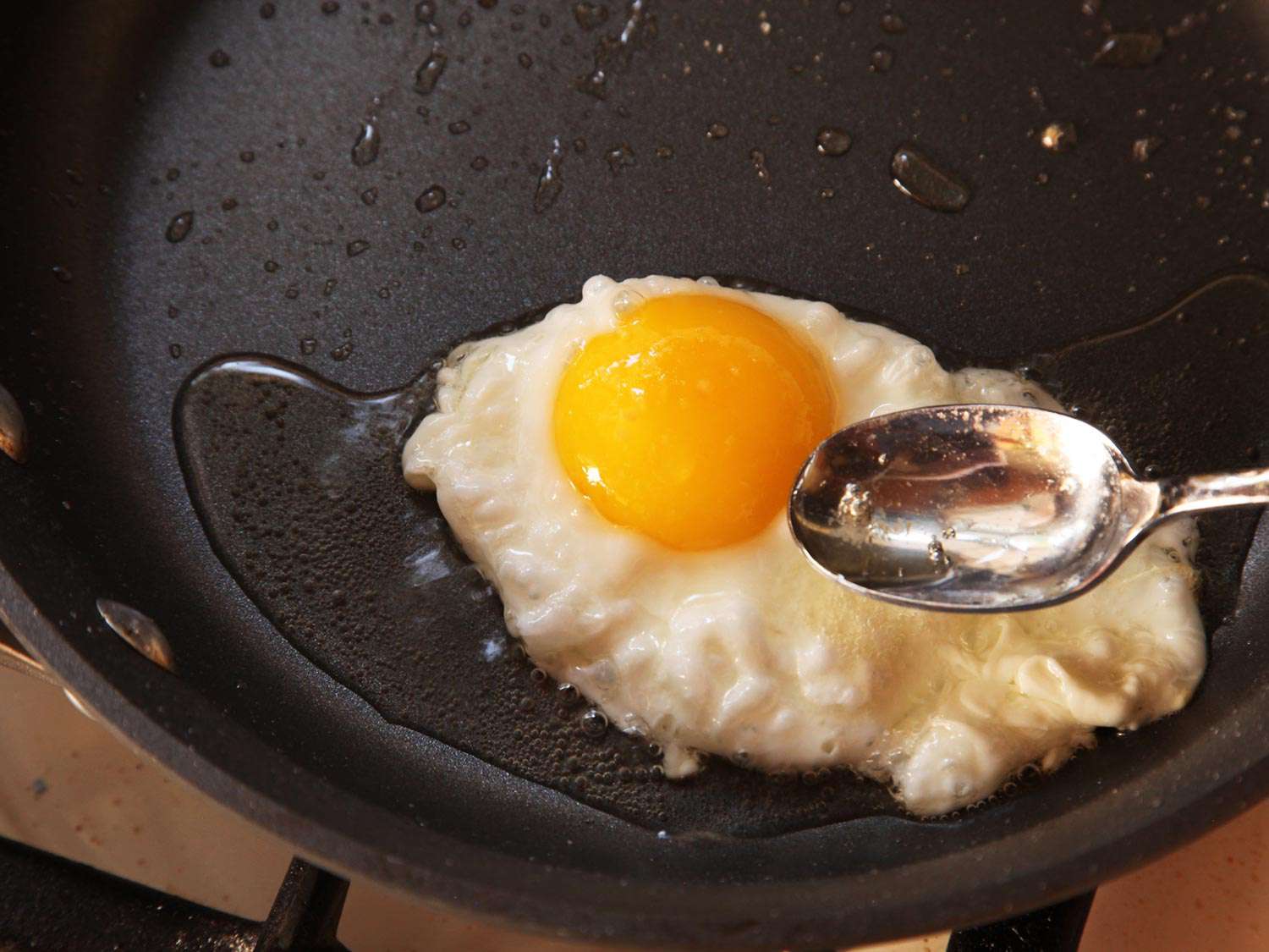 Basting a fried egg with oil for homemade huevos rancheros.