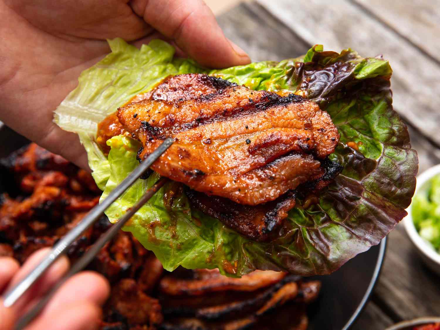 A closeup of the author cradling a piece of dwaeji bulgogi in a lettuce leaf.