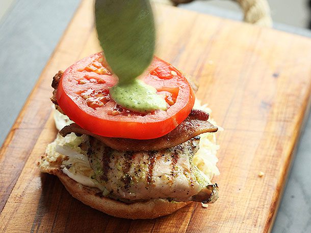 Author balances a thick slice of tomato on top of the bacon slices and applies green sauce to it.