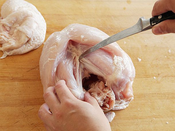 Using a boning knife to cut along the sides of the wishbone in a whole, bone-in turkey breast with its skin removed.