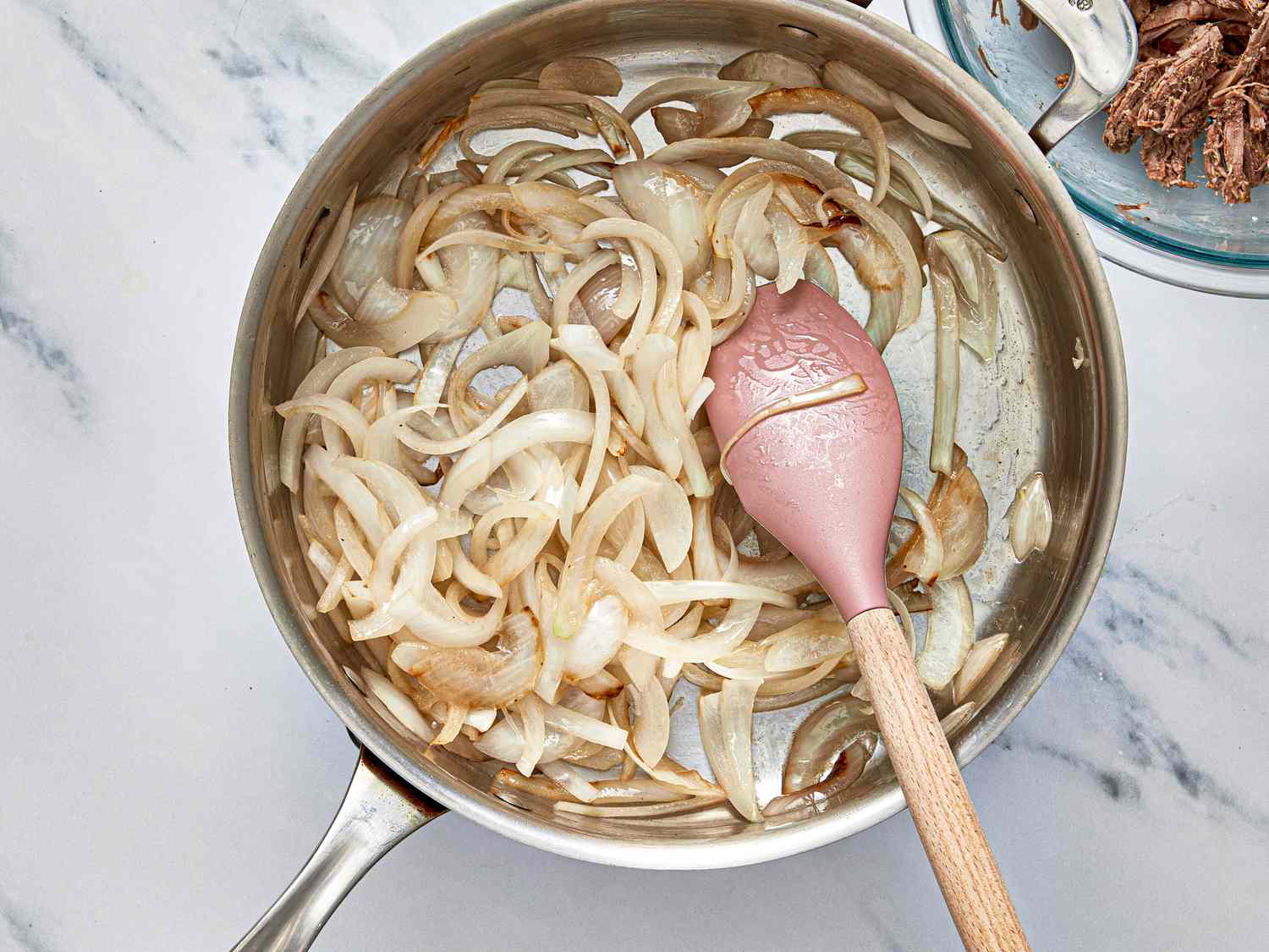 Sauted onions in a skillet with a pink spoon