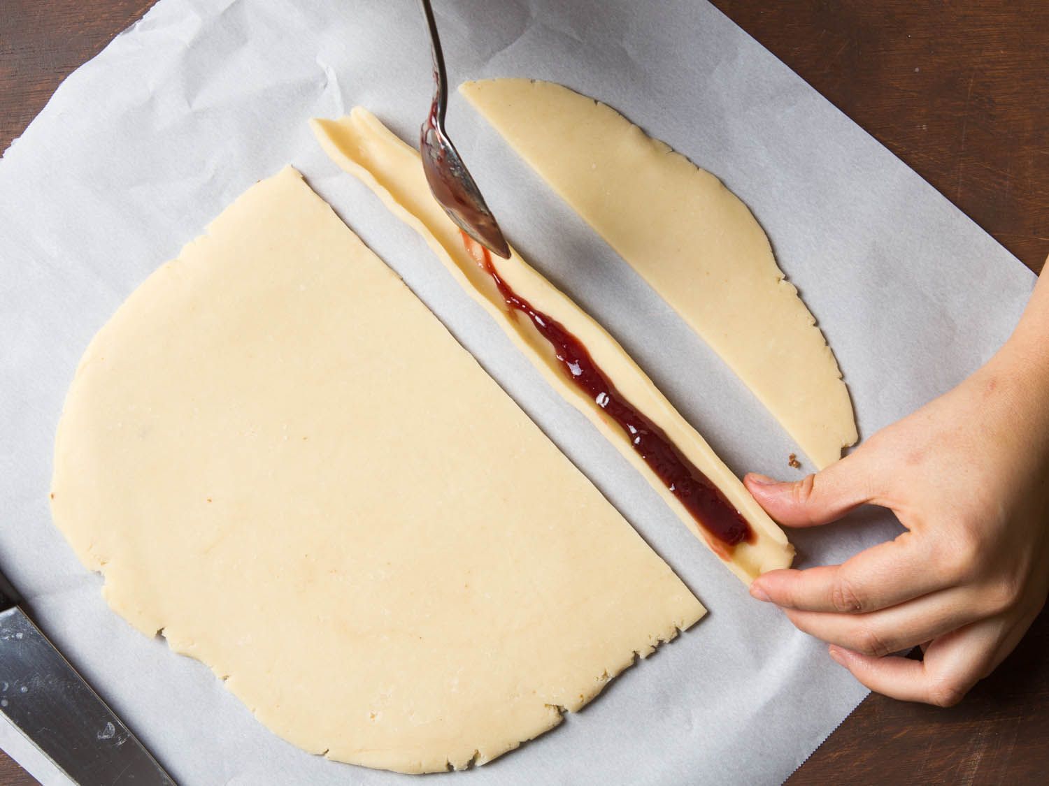 Folding shortbread dough lengthwise and filling the trough with raspberries jam. 