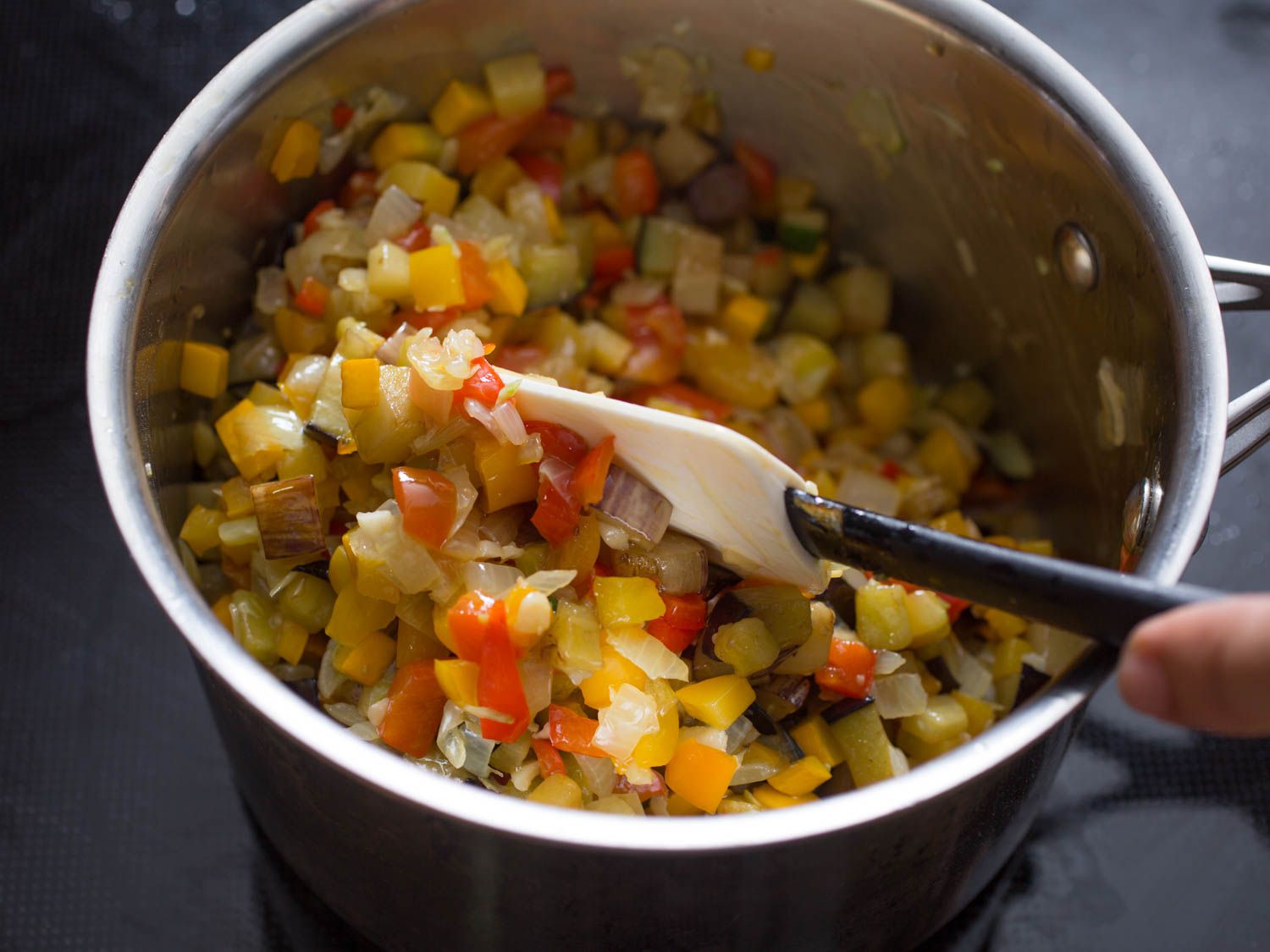 Author stirring the cooked, diced vegetables in a saucepan with a spatula.