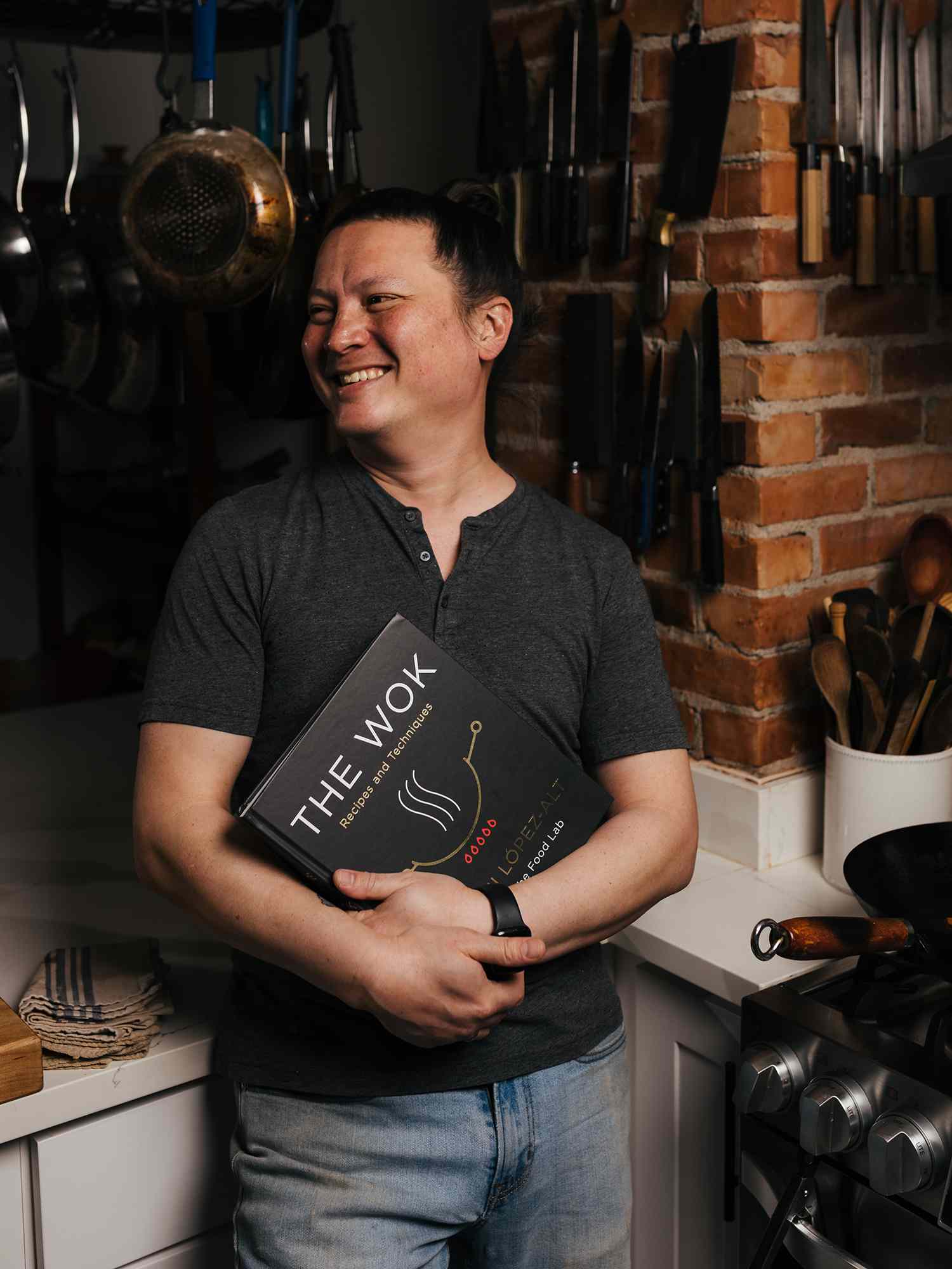 A portrait of J. Kenji LÃ³pez-Alt holding his new book, The Wok, in his Kitchen