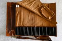 An opened Rustic Town Genuine Leather Chef Knife Roll with compartments a strap and a small pouch on a textured surface