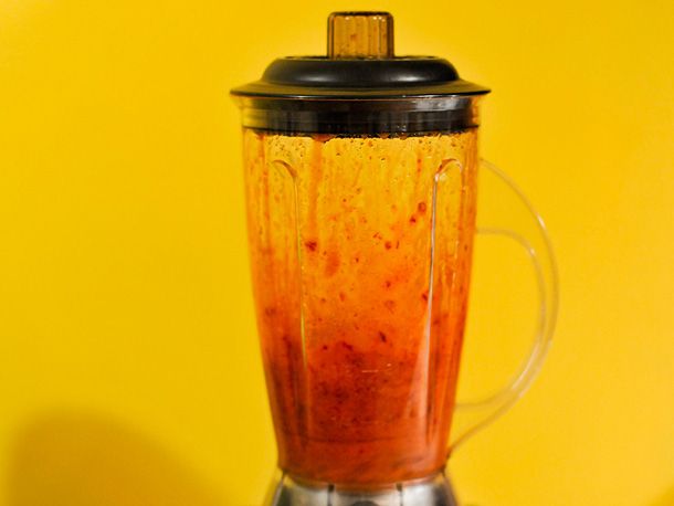 A blender in front of a yellow background holding the sauce.