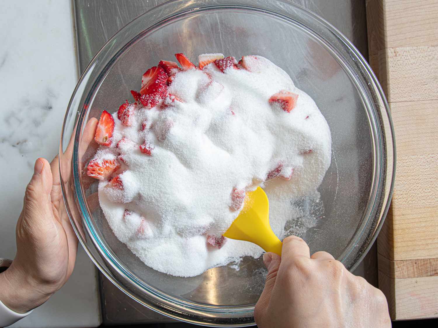 Hands mixing strawberries and sugar in a bowl