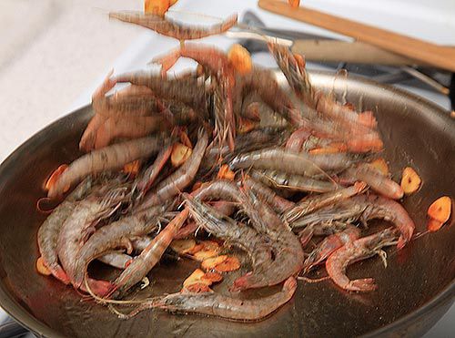 Head-on shrimp are added to the pan and tossed in the air as they cook.