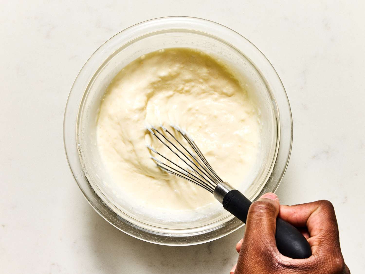 Hand whisking a creamy mixture in a glass bowl