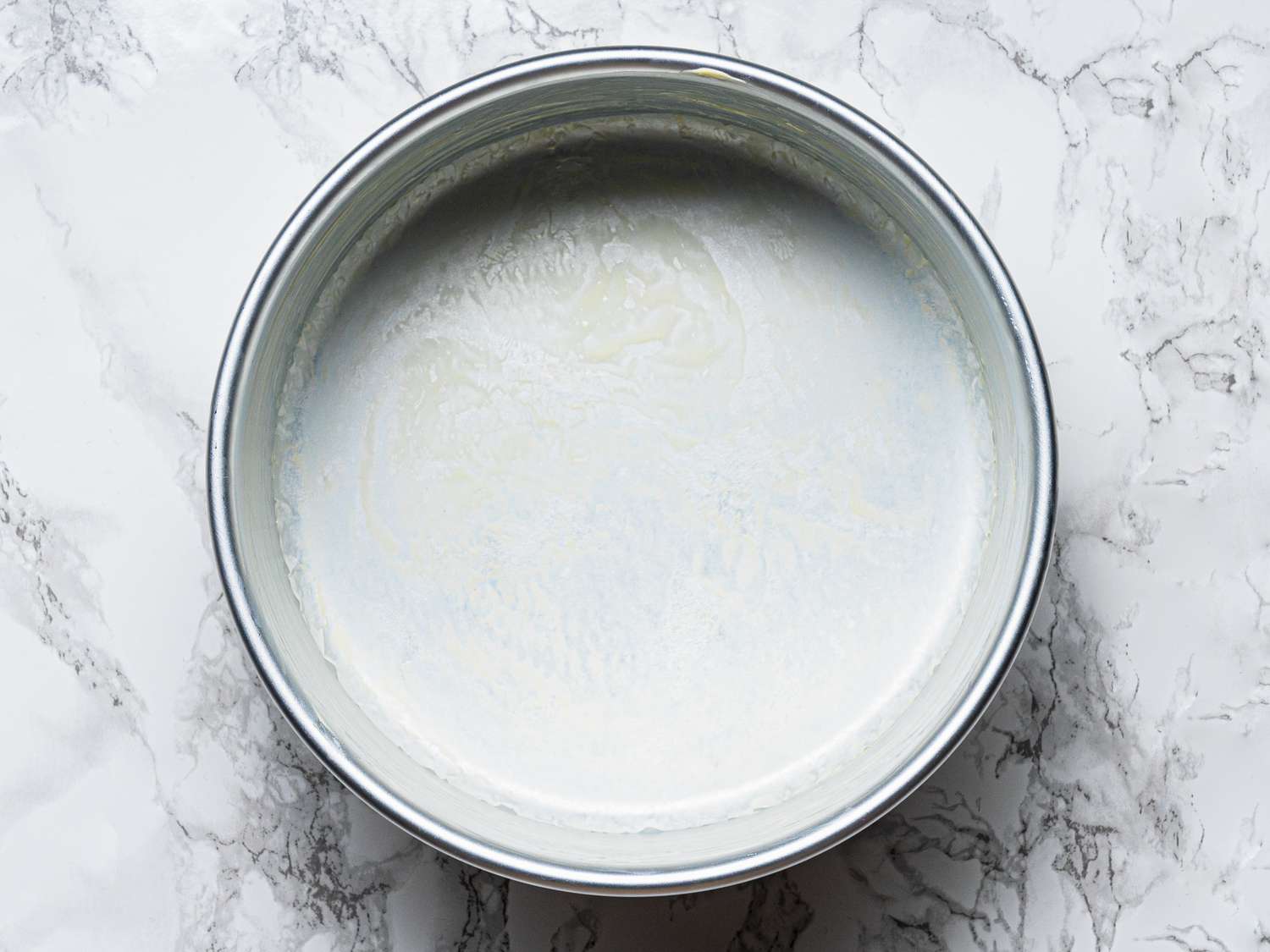Greased round cake pan on a marble surface