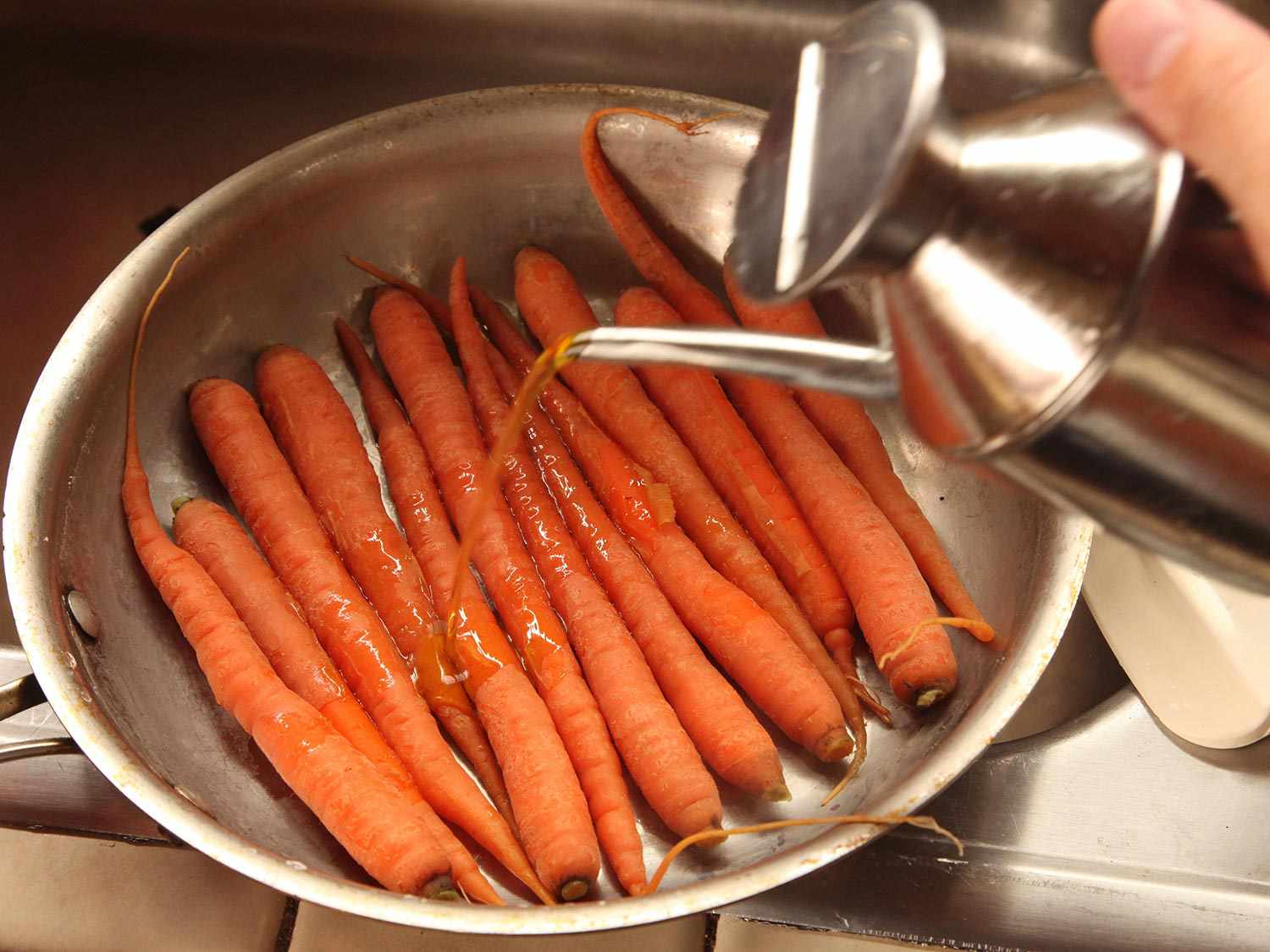 Pouring olive oil on par-cooked carrots in skillet.