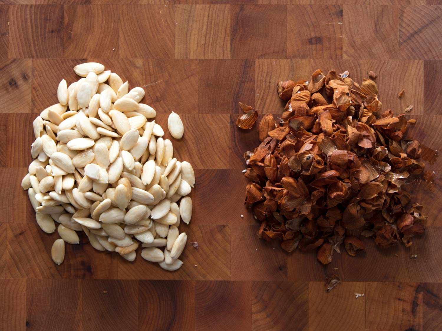 Overhead view of blanched almonds and their skins on a cutting board.