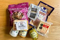 A selection of food items from Cheese Grotto Monthly Cheese Subscription including olives mustard cheese and cured meat on a wooden surface