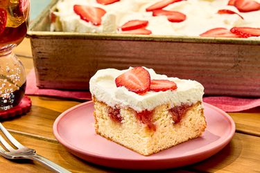 A piece of strawberry poke cake on a plate tray with more in the background