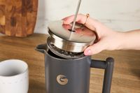 A person adding a lid to the Coffee Gator French press.