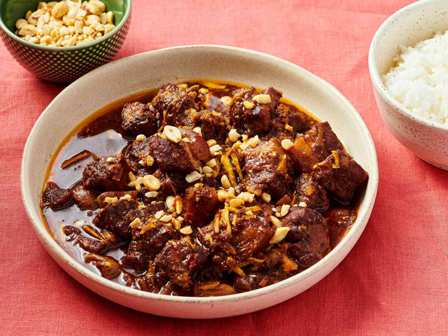 Stew in a bowl with small dish of peanuts and rice in bowl to the side. 