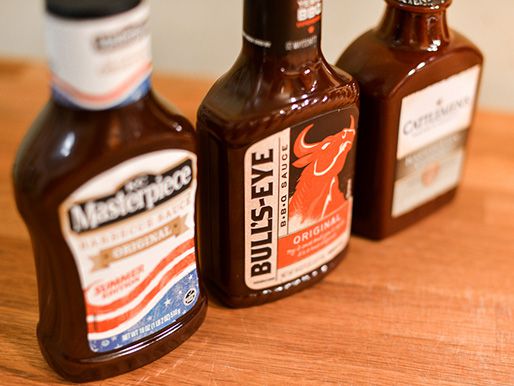Three bottles of store-bought barbecue sauce lined up on a wooden table.