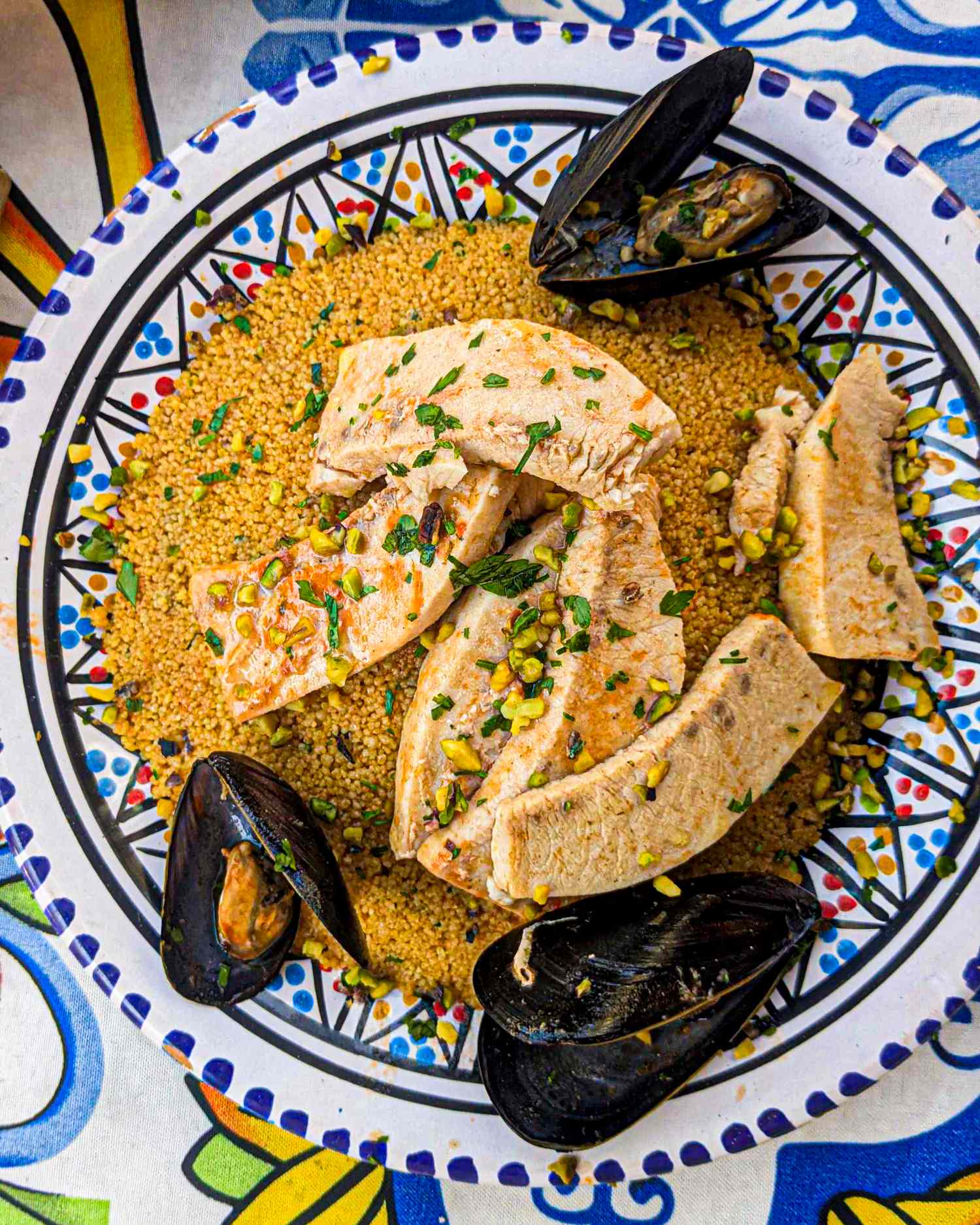 A closeup of a plate of food with couscous mussels and sliced fish pieces garnished with herbs This appears to be a dish of seafood