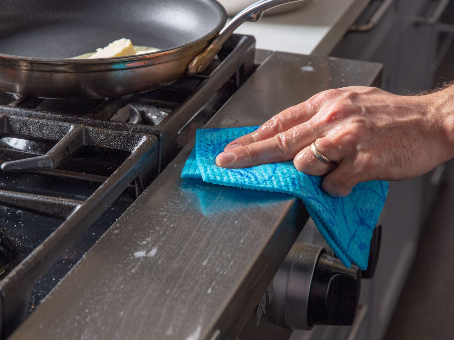 Hand using a Swedish dishcloth to wipe down the front of a stove.