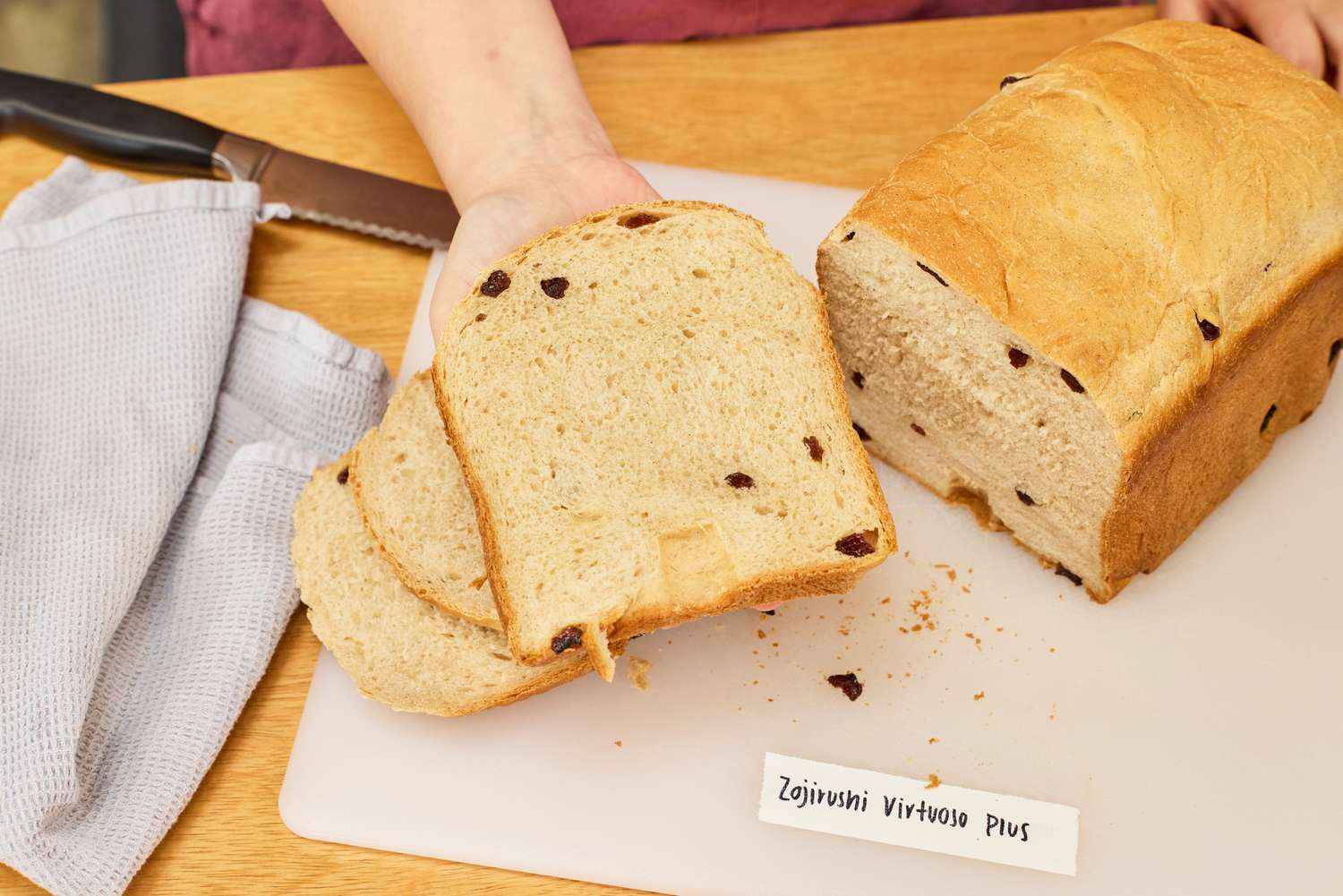 A hand holding a slice of bread from the Zojirushi Home Bakery Virtuoso Plus Bread Maker over a cutting board