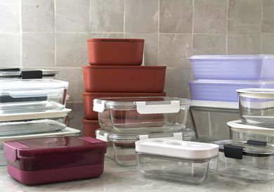 A collection of various food storage containers in different shapes and sizes stacked on a kitchen counter against a tiled backsplash