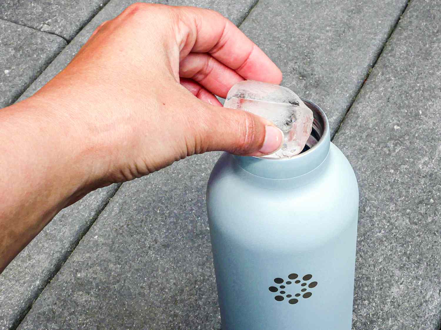 A hand adding ice to a stainless steel water bottle