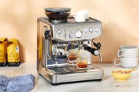The Breville Barista Express Impress brewing coffee into a glass cup on a white marble countertop 