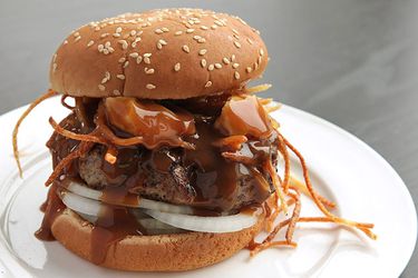 Profile view of a poutine burger, dripping with gravy, served on a white plate.