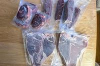 Various cuts of vacuumsealed Omaha Steaks raw meat on a wooden surface including steak cuts and filet portions