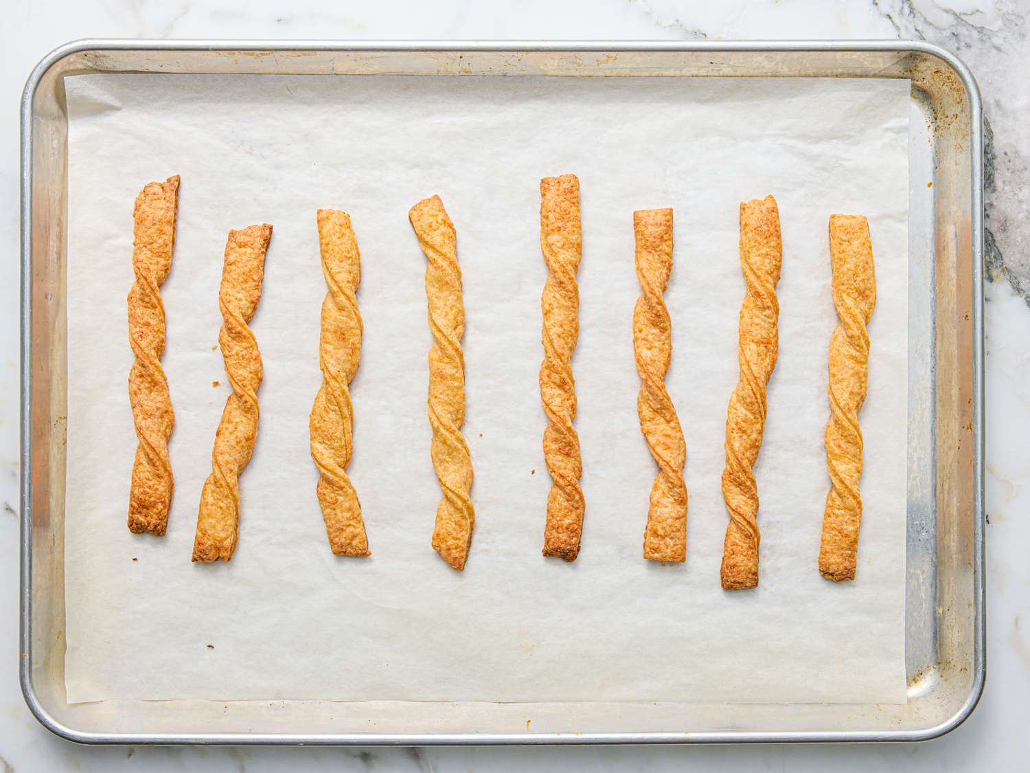 Rows of twisted cheese straws on a parchmentlined baking sheet