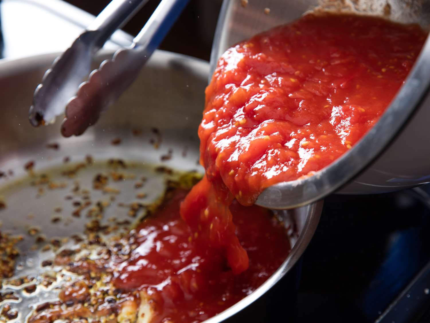 Tomato sauce is poured into the skillet from a prep bowl.