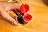 Hand holding a bottle with an open red cap on a wooden surface