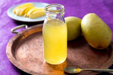 Open bottle of homemade mango syrup with fresh mangoes