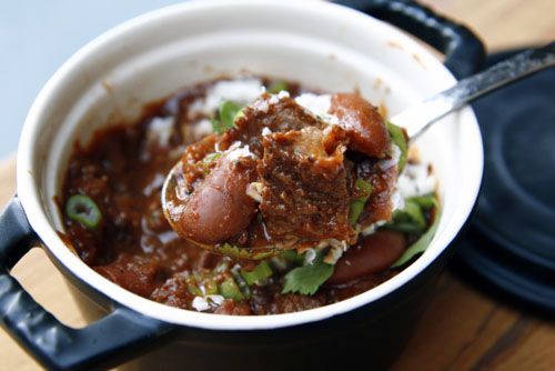 A spoonful of beef chili over a small bowl of chili on a wooden board.