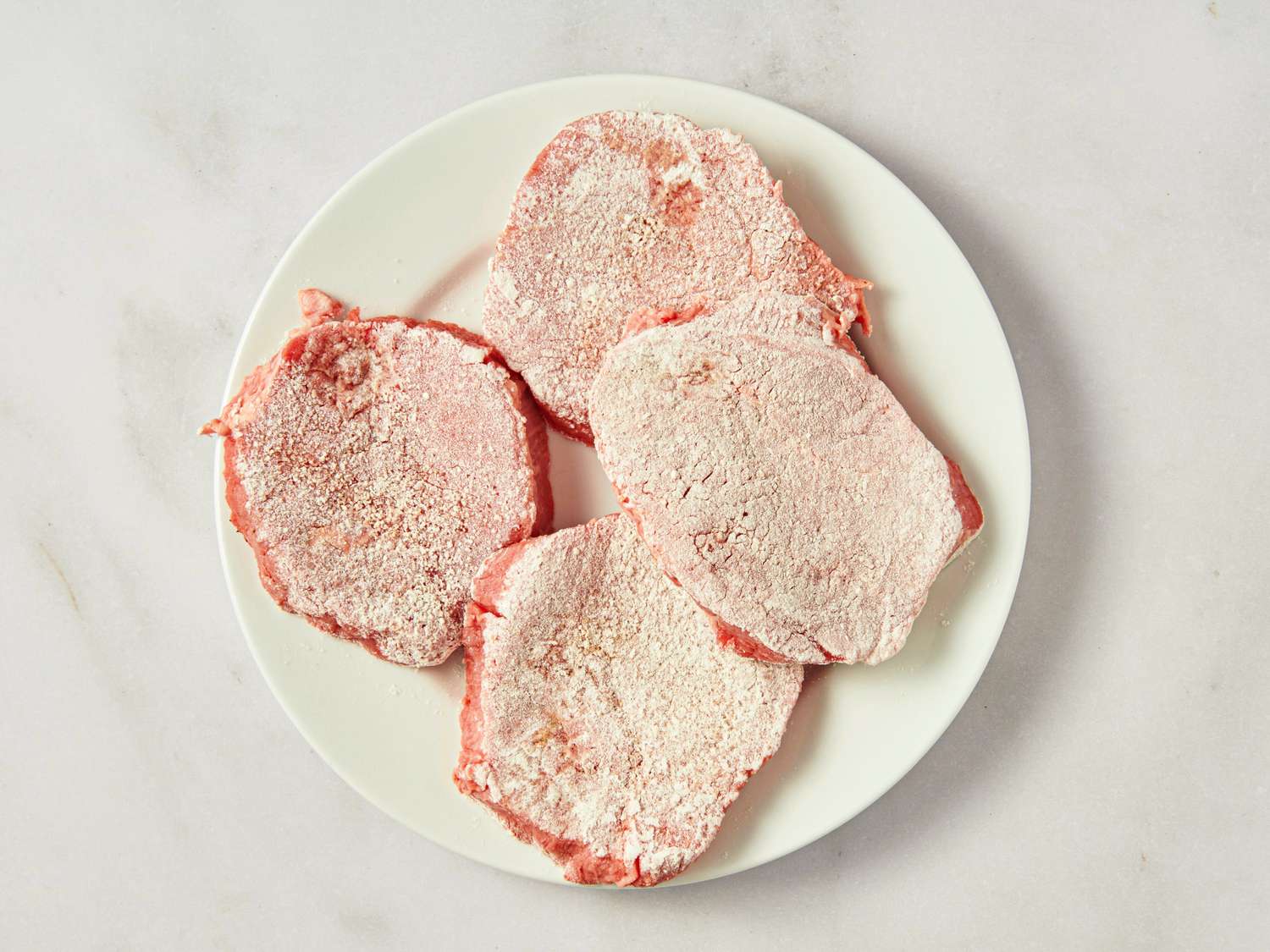 Floured raw beef steaks on a white plate