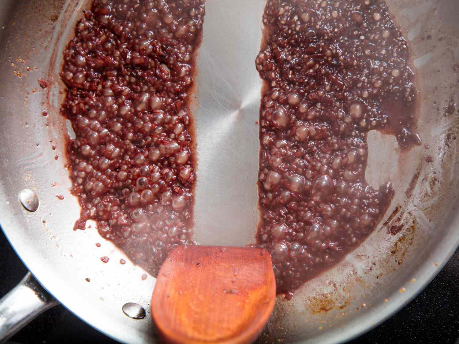 The edge of a wooden spatula drawing across the bottom of a skillet in which a pan sauce is bubbling