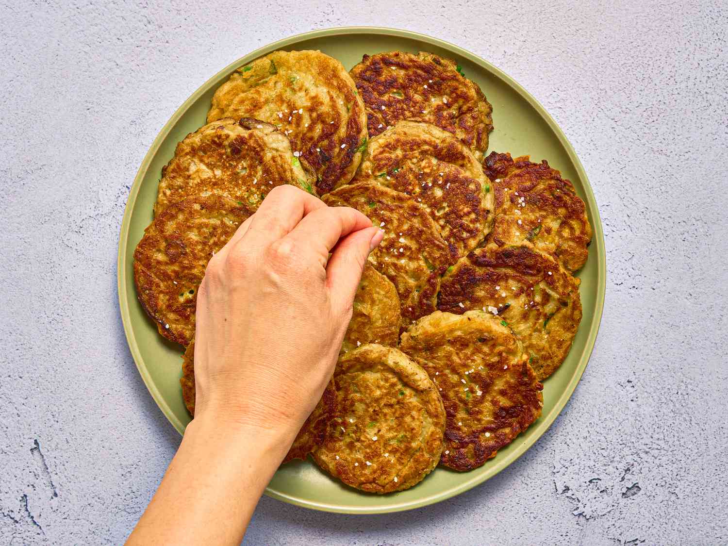 sprinkling salt on fresh made boxty pancakes on a green plate on a stone surface 